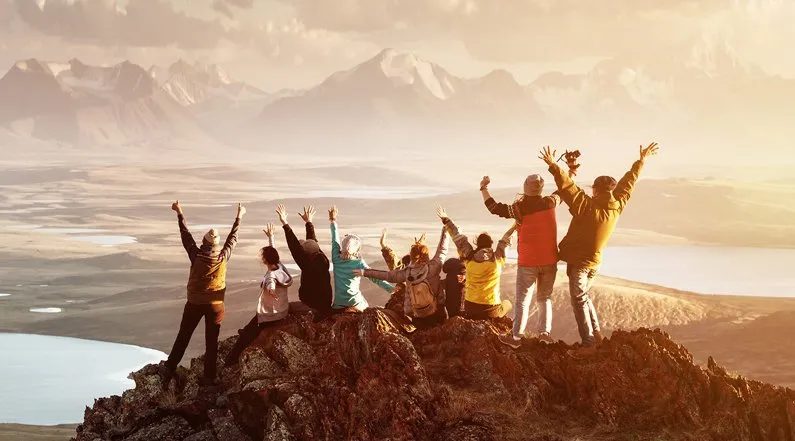 Foto di un gruppo di amici su una montagna con le mani in alto che condividono la passione di viaggiare